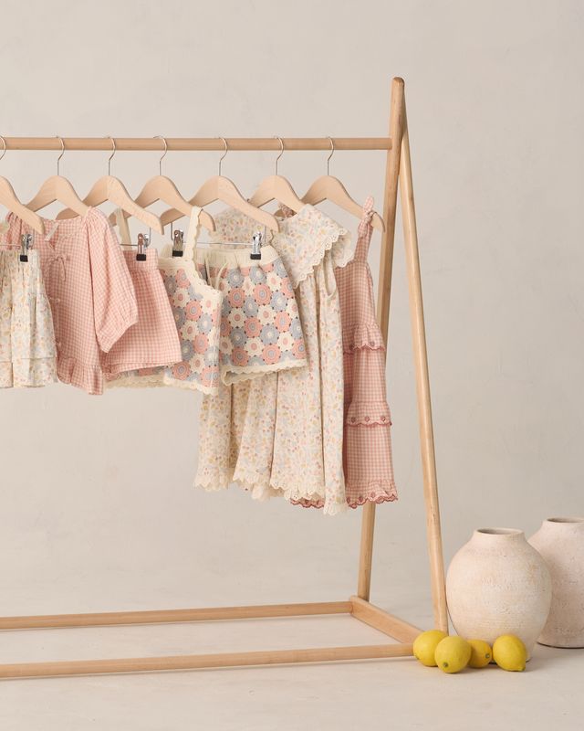 Children's clothing on a wooden rack against a plain wall with decorative elements.