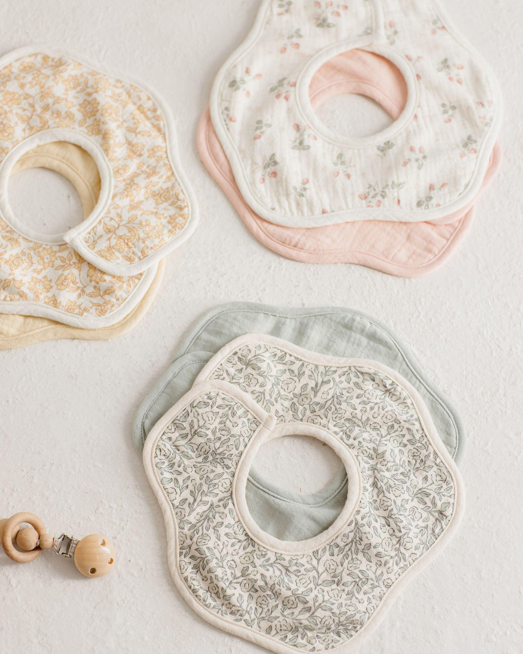 three different sets of bibs in a flower shape. one of them is a sage green print and the other has strawberry print