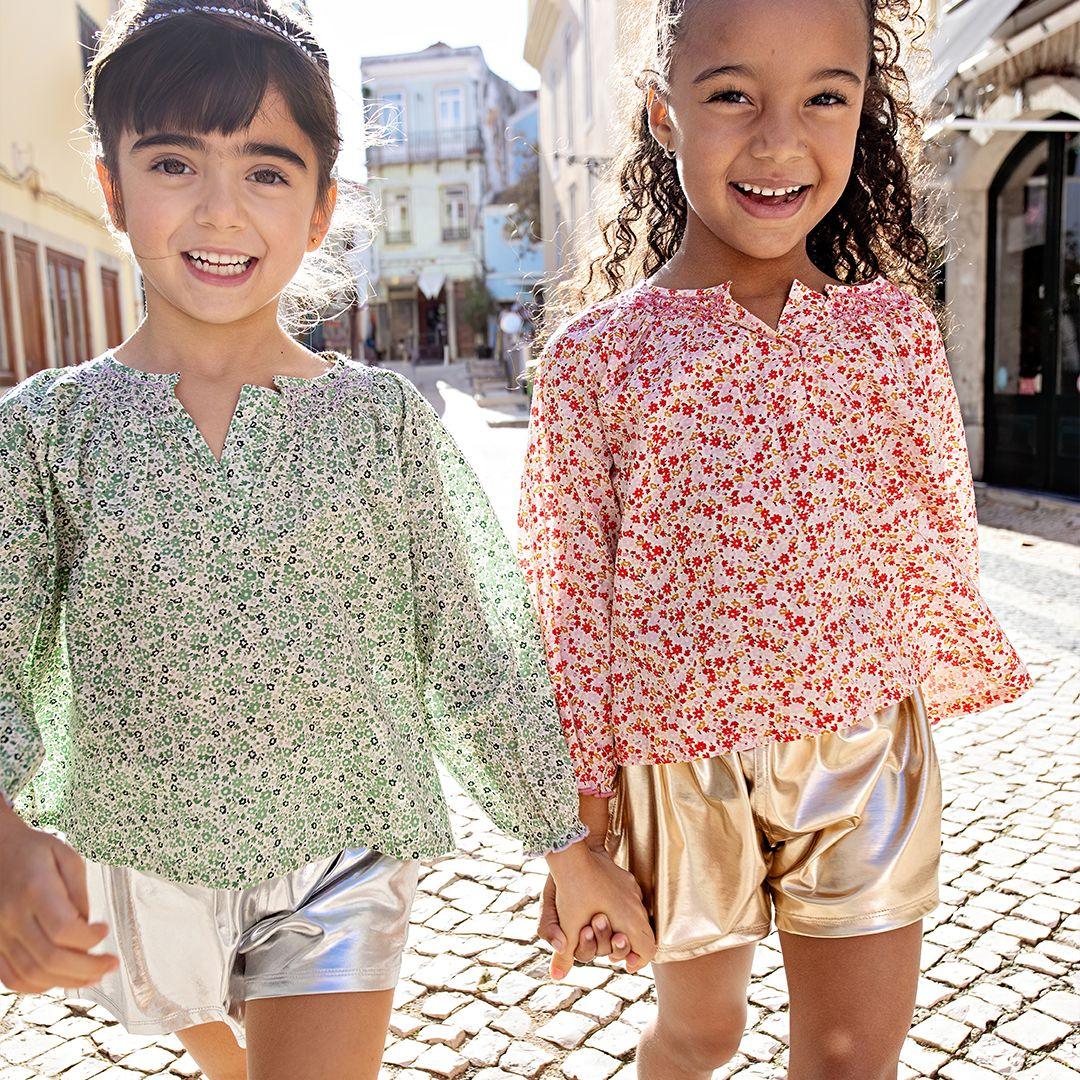 these two girls are are modeling the lame shorts: one silver and one gold each with floral peasant top. the girls are smiling and holding hands. 
