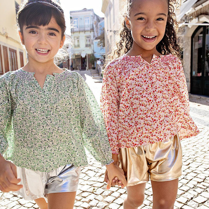 these two girls are are modeling the lame shorts: one silver and one gold each with floral peasant top. the girls are smiling and holding hands. 
