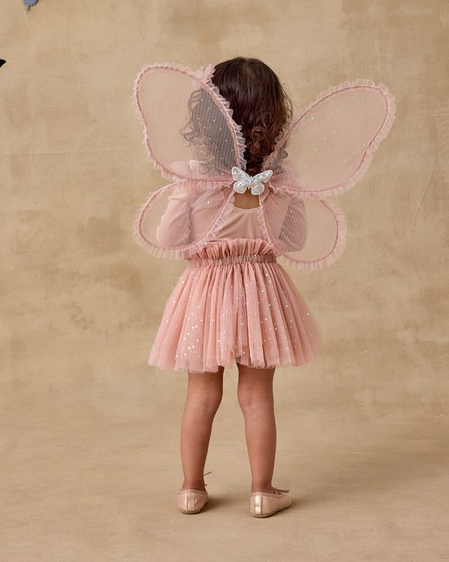 Child wearing a pink fairy costume with wings on a beige background