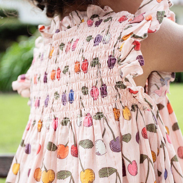 up close look at the print of the dress light pink with multi colored cherries all over it. 