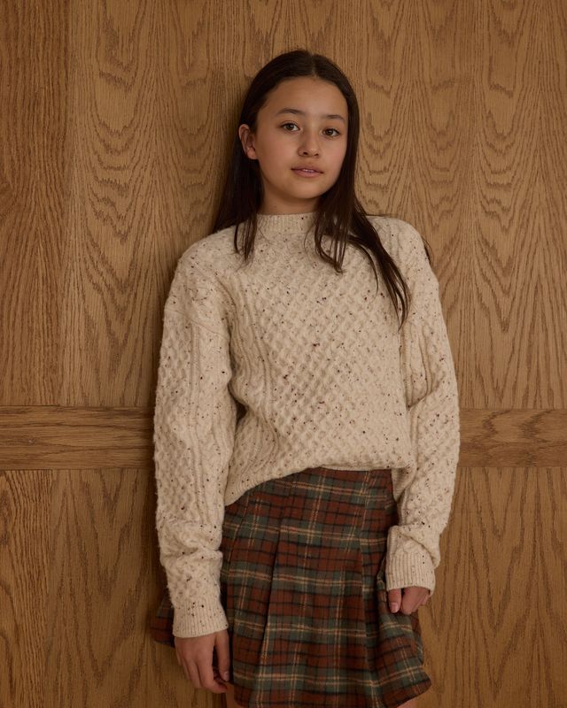 young girl wearing a textured beige sweater and plaid skirt. 