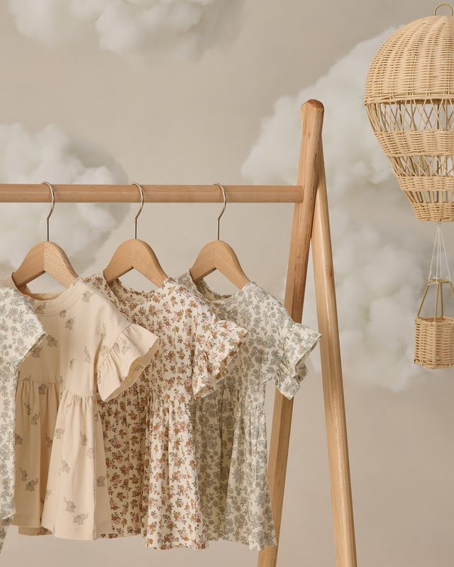 Children's dresses hanging on a wooden rack with a neutral background