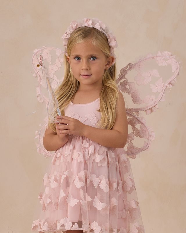 Young girl in a pink butterfly dress with fairy wings and wand against a beige background