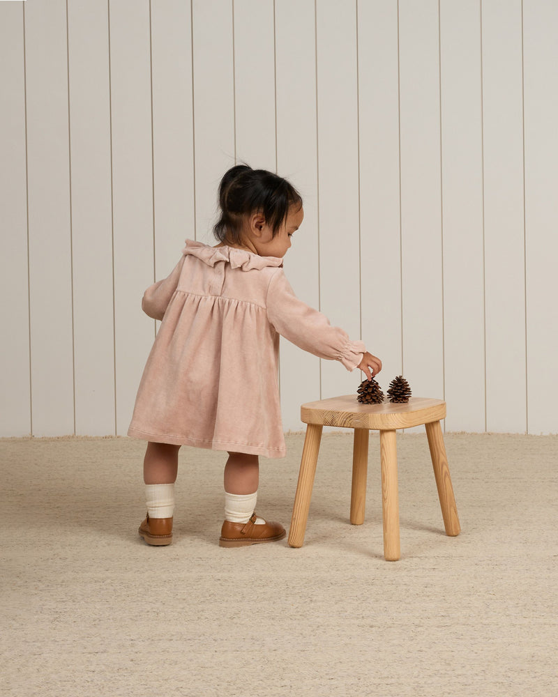 baby modeling the blush velour dress while playing with pine cones 