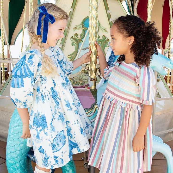 both girls are posing looking at one another and standing from the side. each dress has a puff sleeve and full skirt