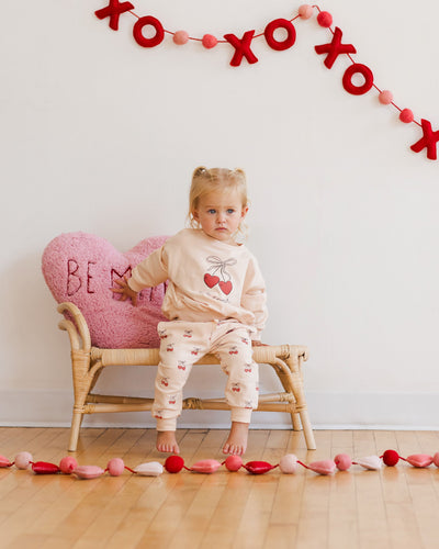 little girl modeling the sweatsuit with cherries on  it. the sweatset is a light pink/beieg in color. cherries on the pants and top