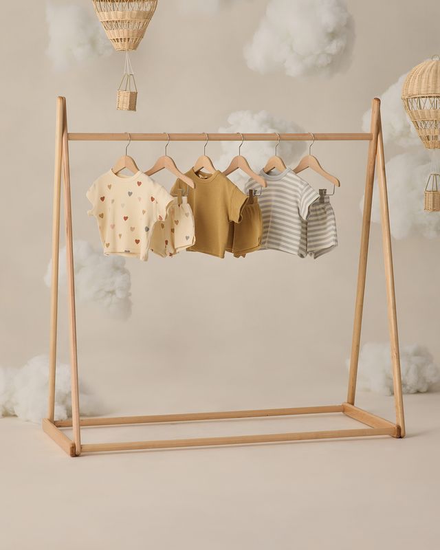 Wooden clothing rack with baby clothes against a neutral background