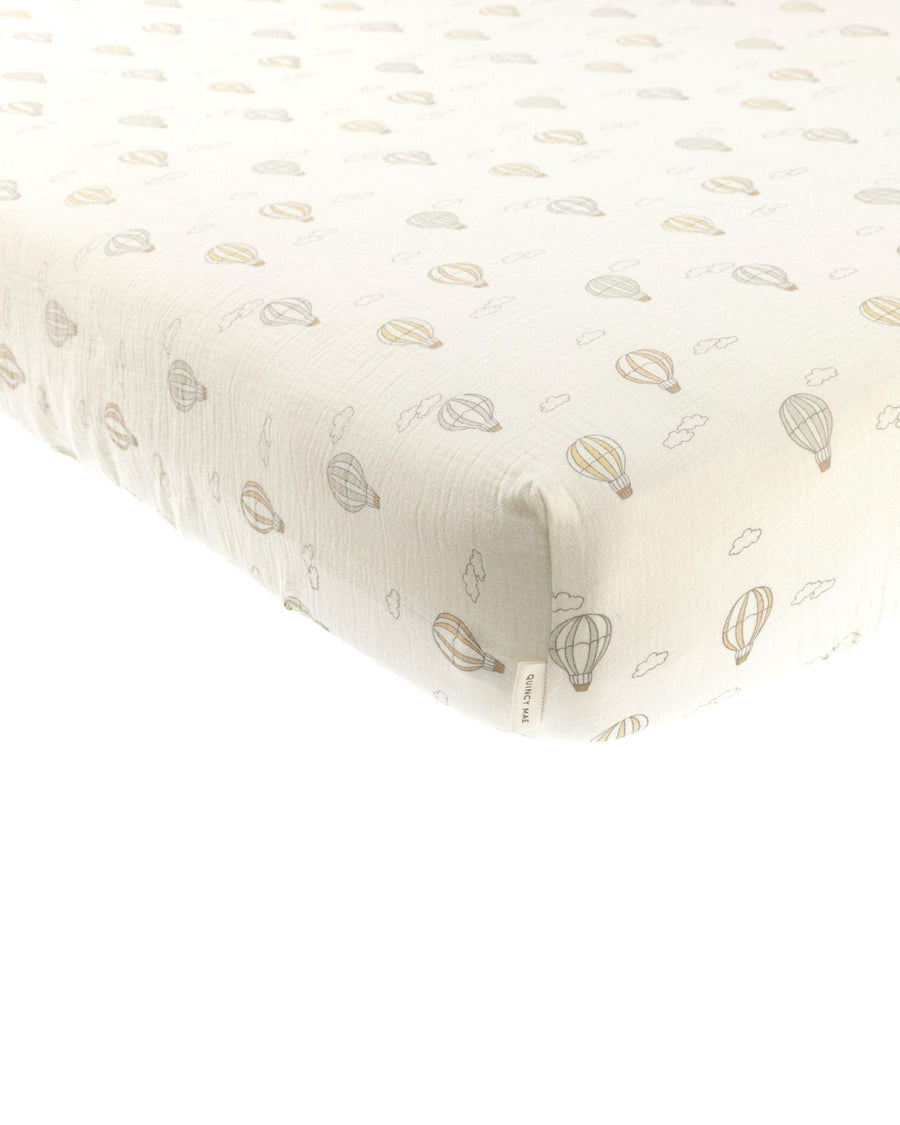 beige crib sheet, woven with hot air balloons printed all over it. 