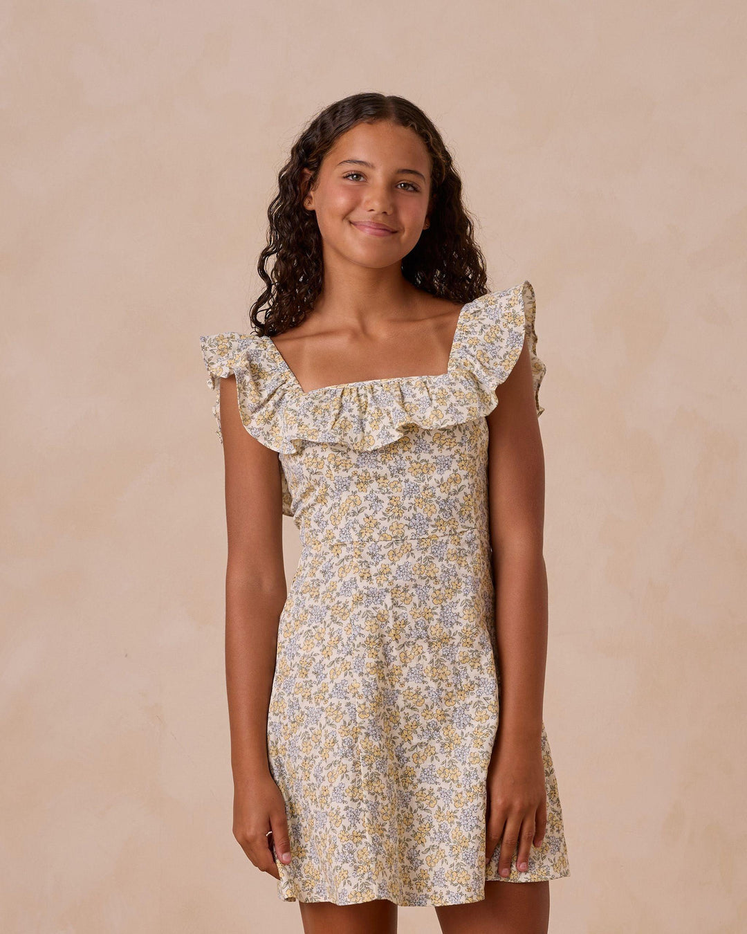 girl modeling a spring dress in the bloom floral print yellow and blue flowers. small ruffle at the neckline. 