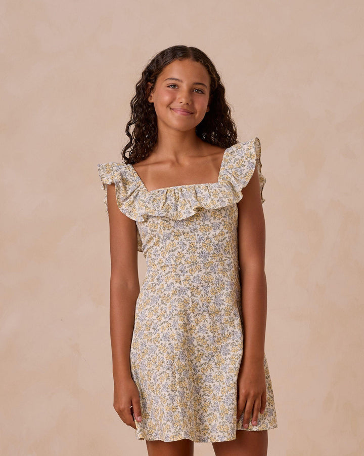 girl modeling a spring dress in the bloom floral print yellow and blue flowers. small ruffle at the neckline. 
