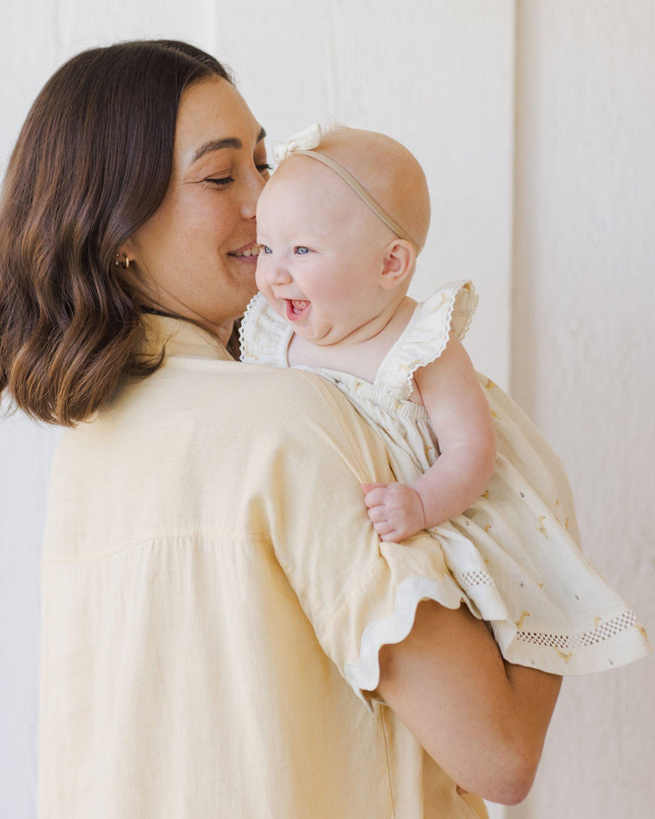 a mom holding the baby in a dress with geese on it. dress has a full body and baby has a big smile on her face