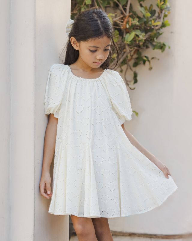 Young girl wearing a white dress with puff sleeves against a neutral background