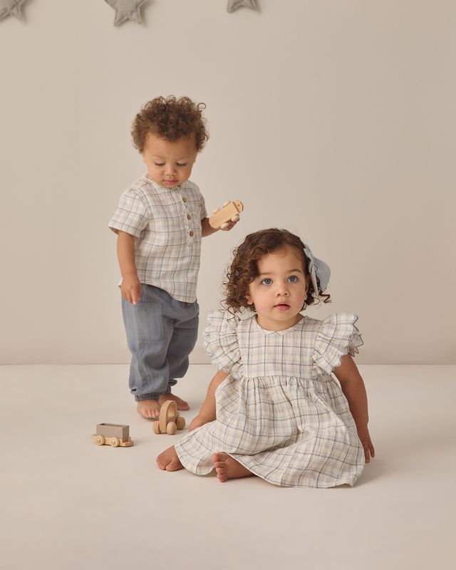 Two children in matching plaid outfits standing on a neutral background