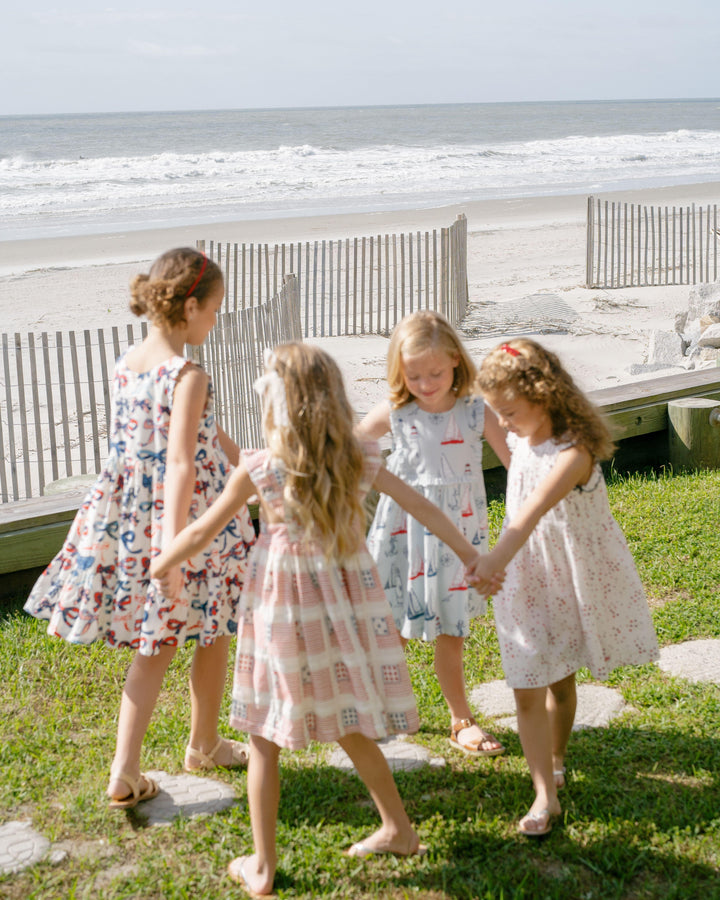 4 little girls holding hands and walking around in circles on the grass in front of the beach. 