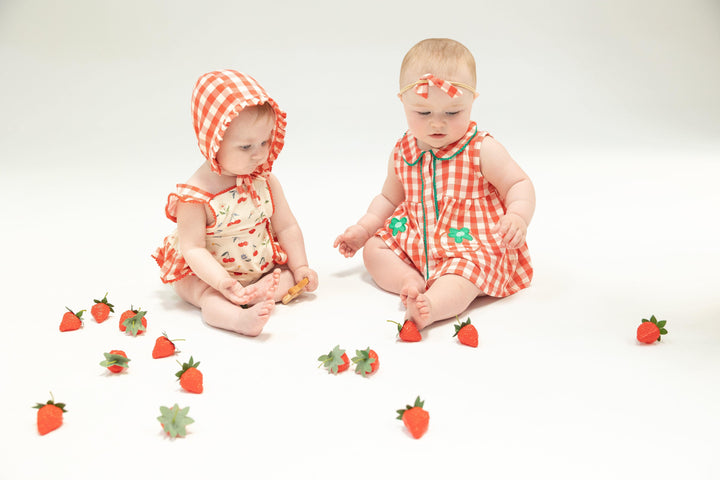 baby modeling the cherry ruffle sunsuit and red and white gingham bonnet. baby modeling the red and white ginham sundress with green daisies on the pocket. 