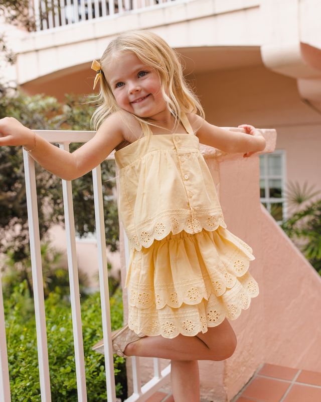 Young girl in a yellow two piece set with eyelet detailing standing on a balcony