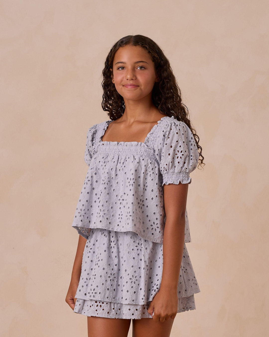 girl modeling light blue eyelet top and skirt. top has puff sleeves and two tiers of eyelet material. 