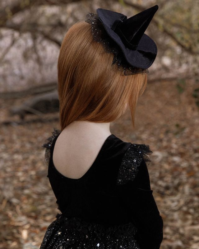 Person wearing a black dress with a decorative headpiece against a natural background