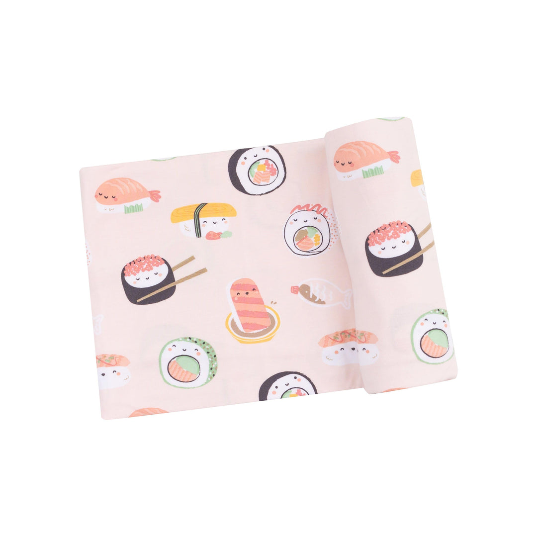 baby swaddle with sushi printed on it on pink ground. the sushi has little faces all over it. 