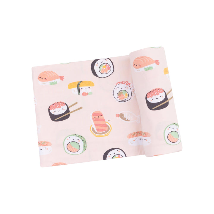 baby swaddle with sushi printed on it on pink ground. the sushi has little faces all over it. 