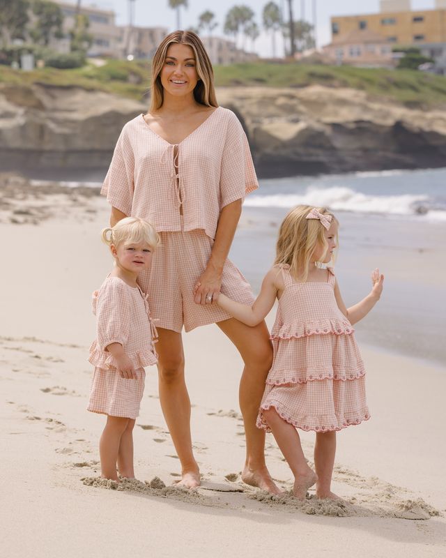Woman and two children in matching pink outfits standing on a beach.