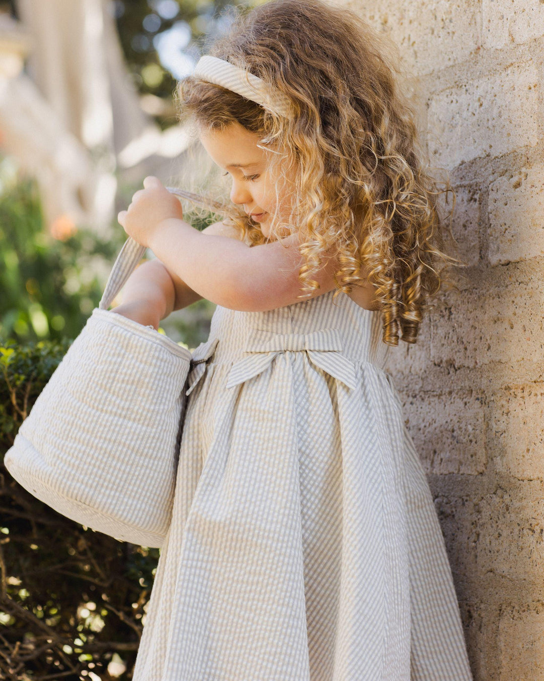 little girl looking through her easter basket. sage stripe dress with two bows in the front, textured fabric 