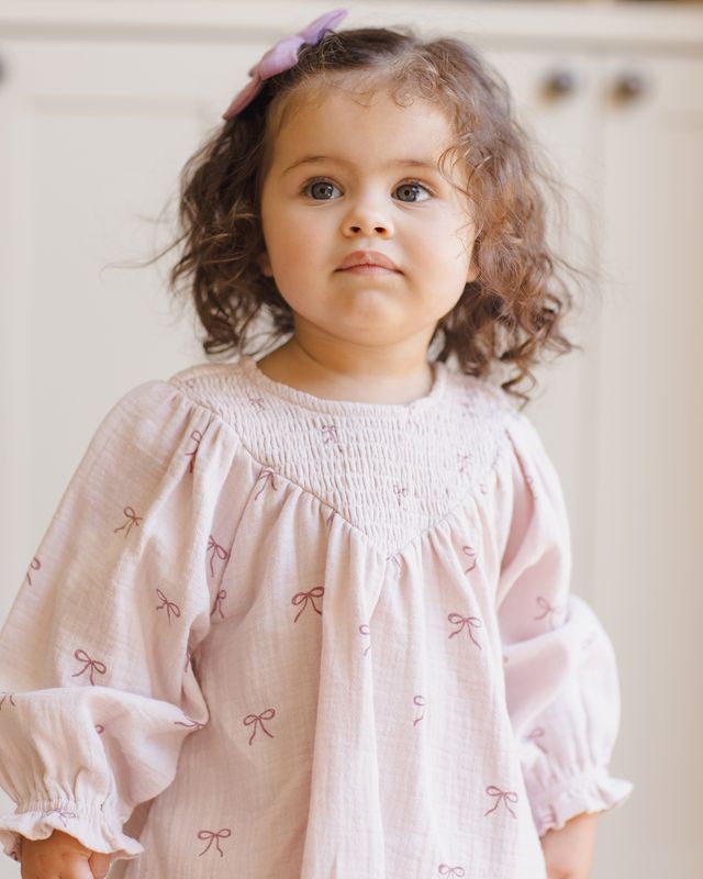 Young child wearing a light pink dress with bow patterns against a neutral background