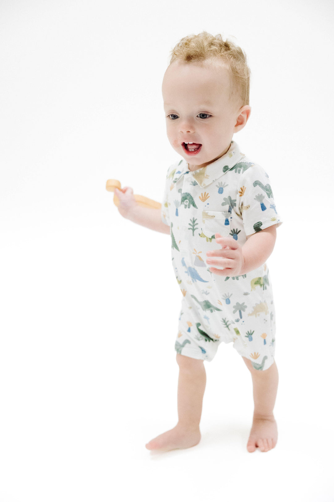 baby boy modeling the polo shortie with soft pastel dinsosaurs printed on it. 