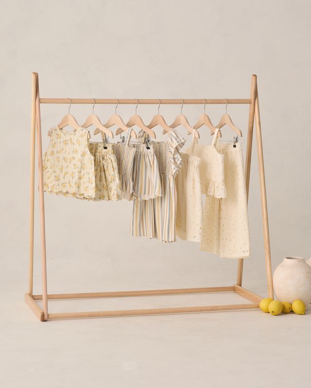 Wooden clothing rack with baby dresses on a neutral background