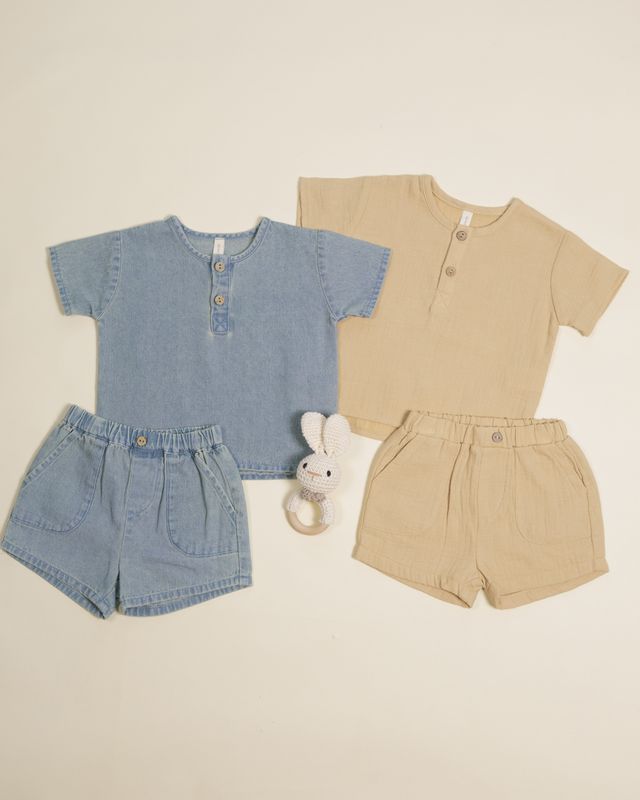 Two children's outfits, one in blue and one in beige, with matching shorts and a toy on a beige background.