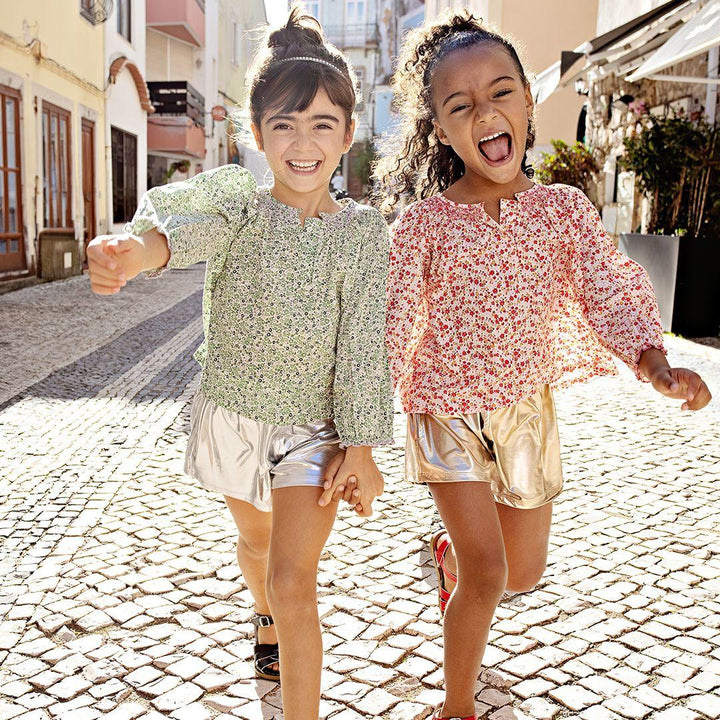 two girls modeling the lame shorts: one silver and one gold. each girl is laughing and wearing a floral peasant top with the shorts. 