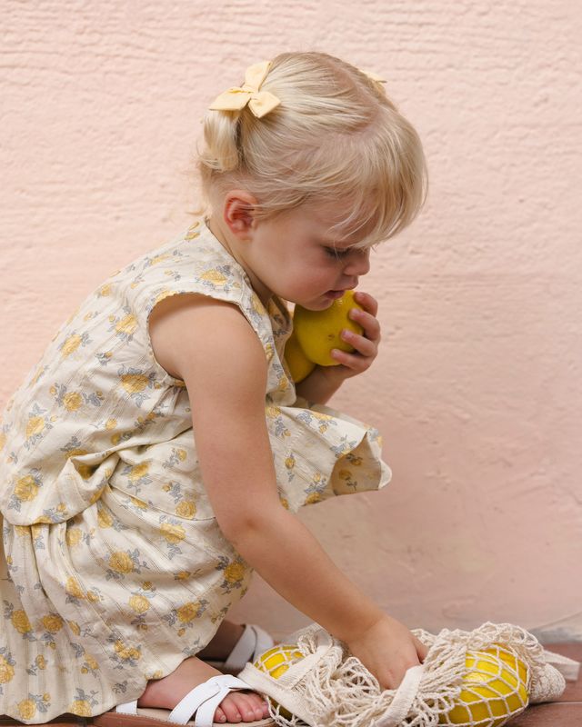 Young girl in a floral dress holding a yellow ball against a pink textured wall.