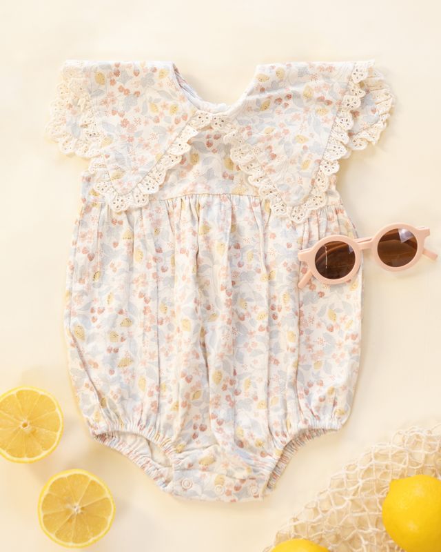 Floral baby romper with ruffled collar on a light background with lemons and sunglasses.