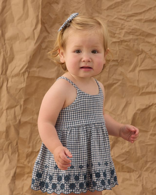 Young child wearing a navy checkered dress against a brown backdrop