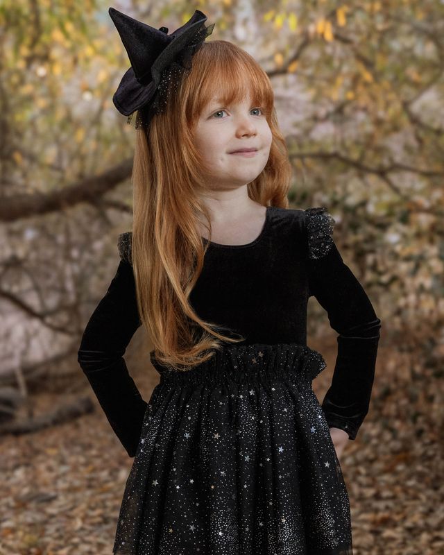 Young girl in a black dress with a witch hat against a natural background