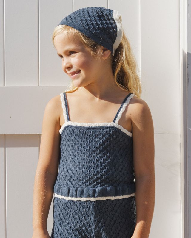 Young girl wearing a blue knitted dress and headband against a light wooden panel background