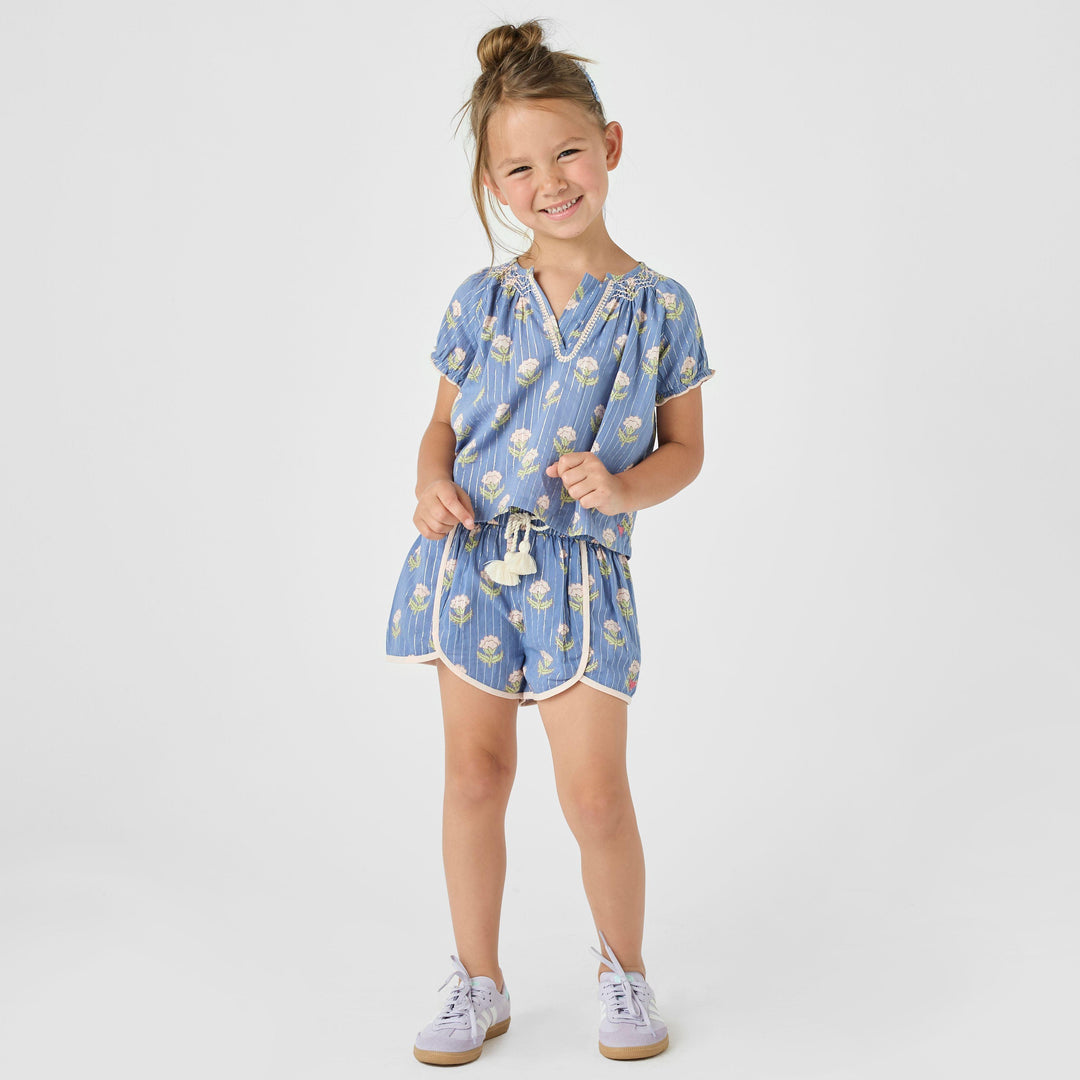 little girl modeling a matching blue top and shorts with a floral pattern on the top and shorts -- silver lurex running through it. 