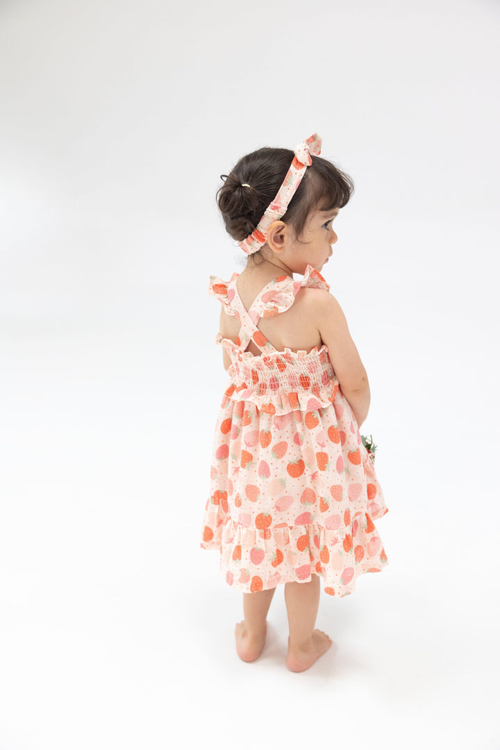 little girl modeling the starwberry dress showing the back has criss cross straps and a ruffle at the bottom. 
