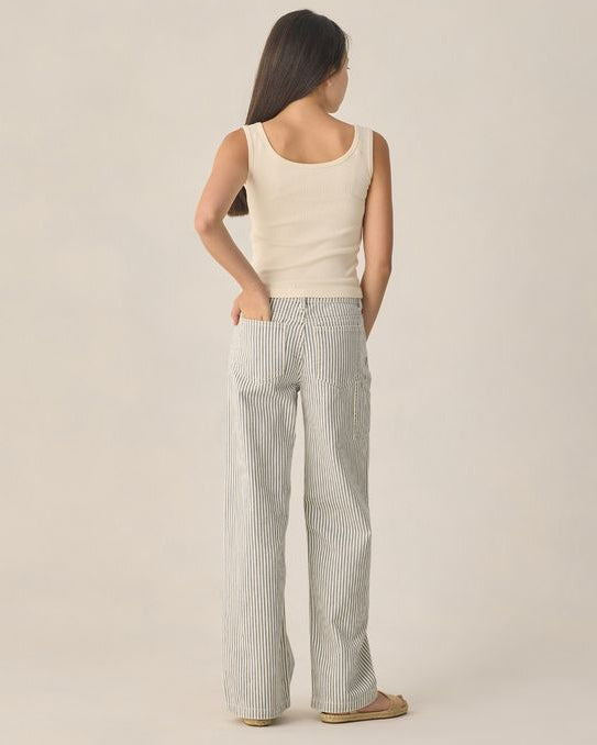 Young Woman wearing a cream tank top and striped pants against a beige background