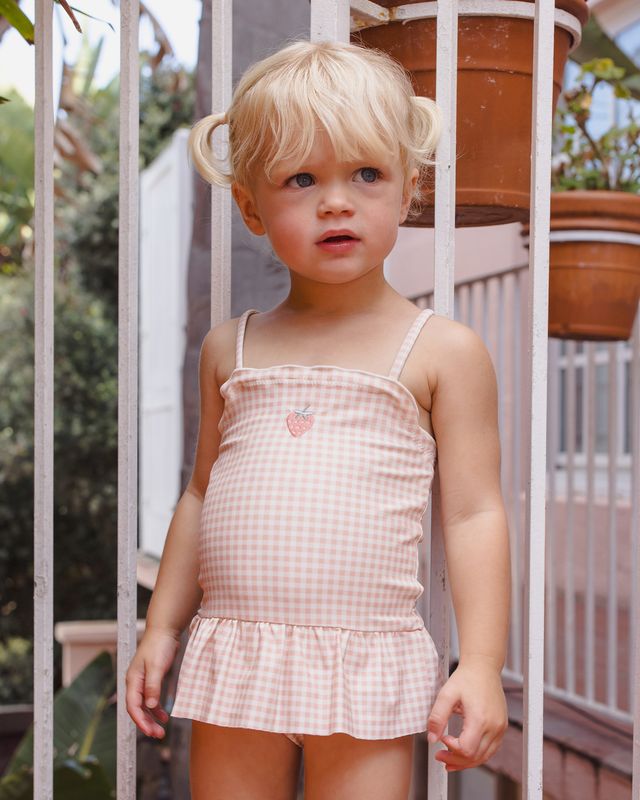 toddler wearing pink gingham bathing suit with small strawberry in the center of the chest. 