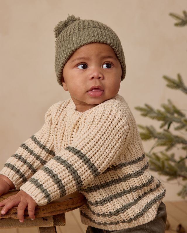 Baby wearing a striped sweater and knit hat with a neutral background
