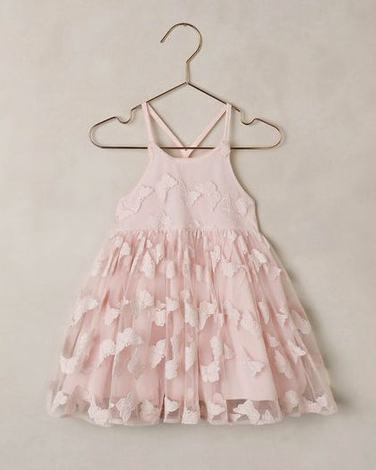 Pink butterfly dress on a hanger against a beige wall