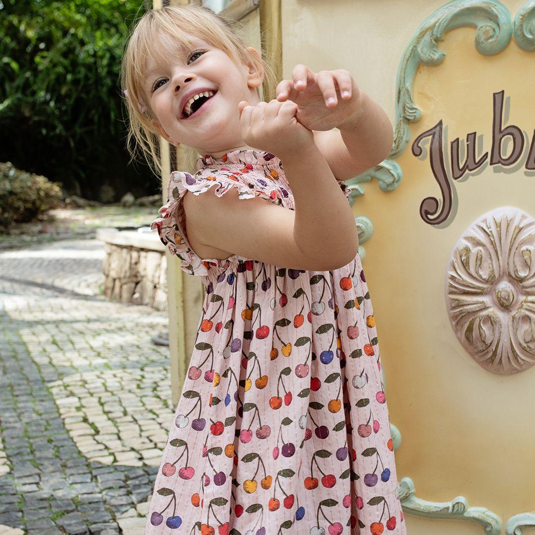 little girl modeling the pink dress with multi colored cherries all over it. she is happy and laughing !