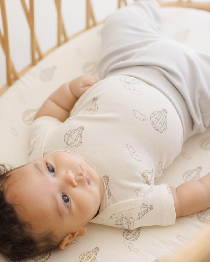 baby laying in a crib on the hot air balloons crib sheet. 