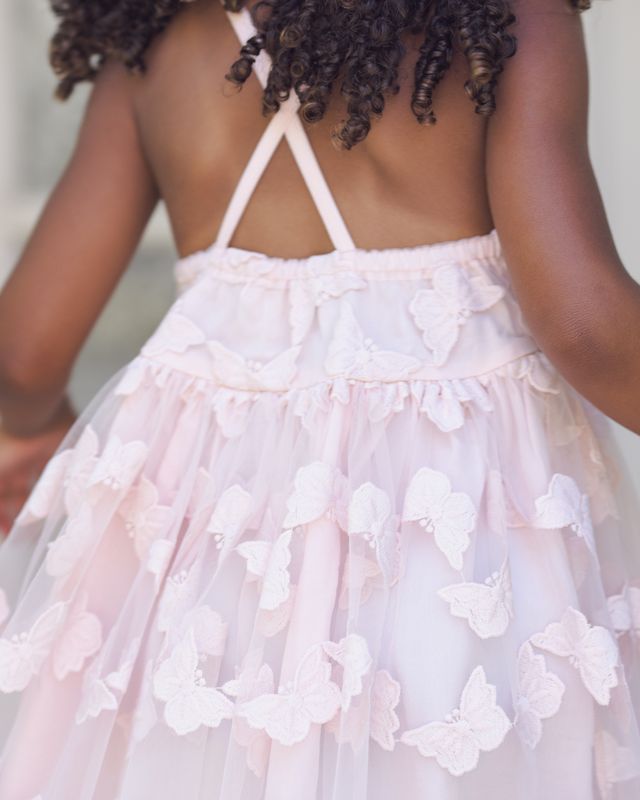 Back view of a child wearing a light pink dress with buttefly details.