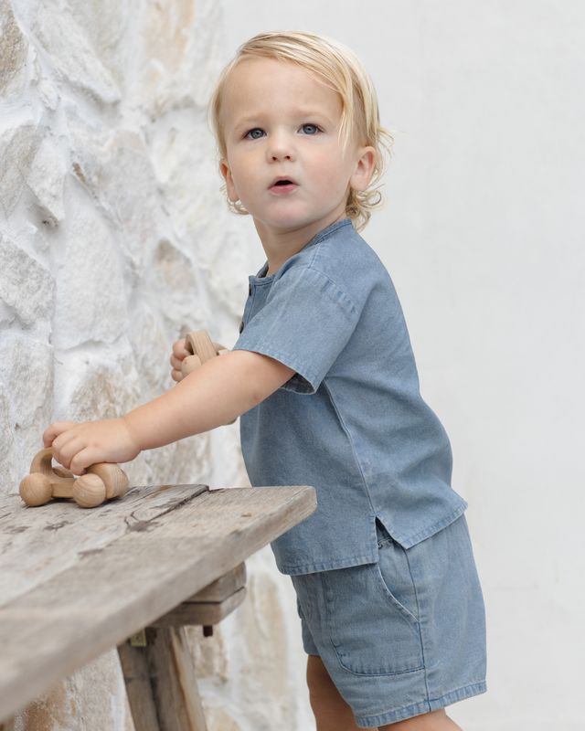 Child in a denim outfit playing with wooden toys against a neutral background