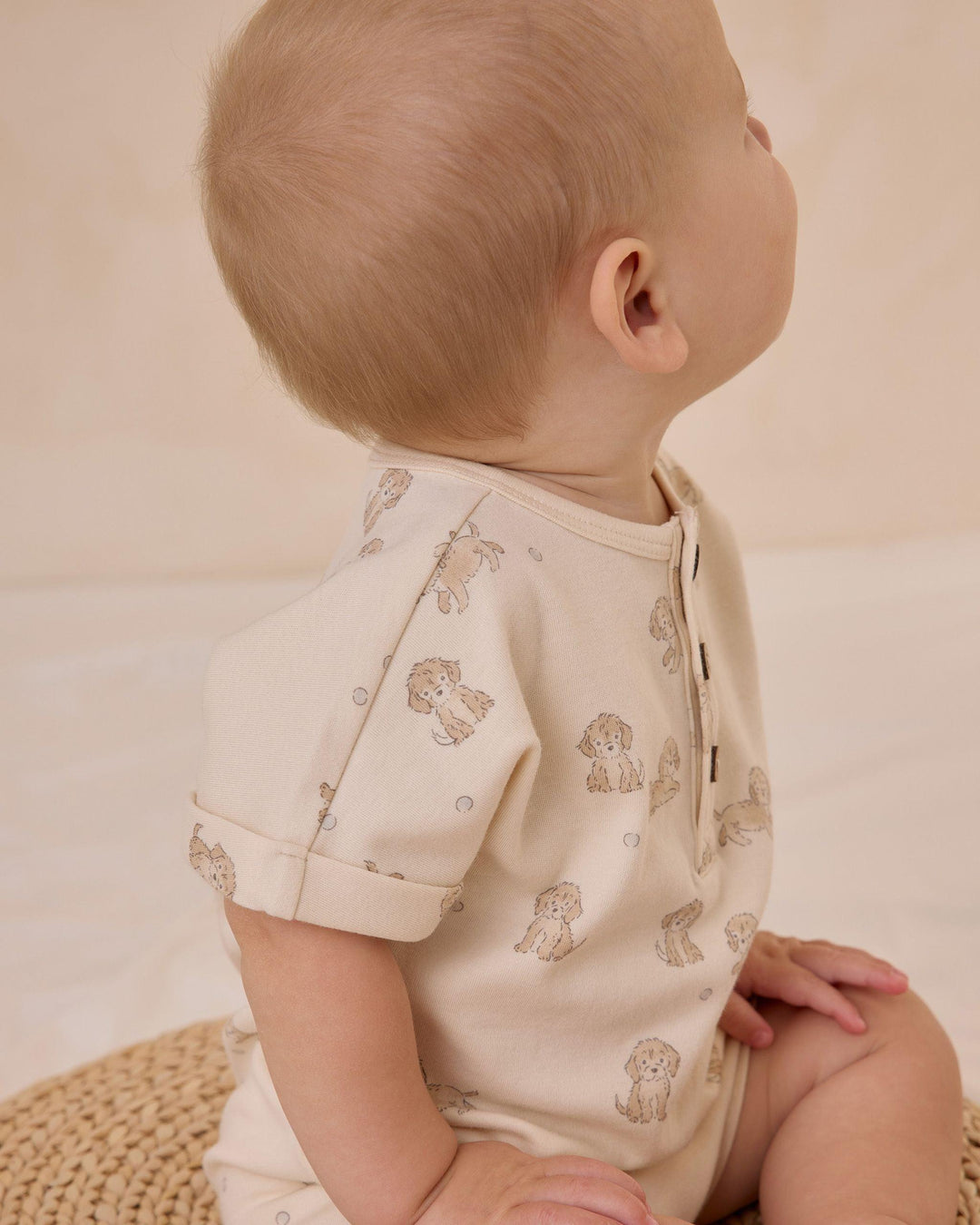 baby modeling the short sleeve baby romper with tiny puppies all over. this picture shows an up close look at the sweet puppy on the sleeve. 