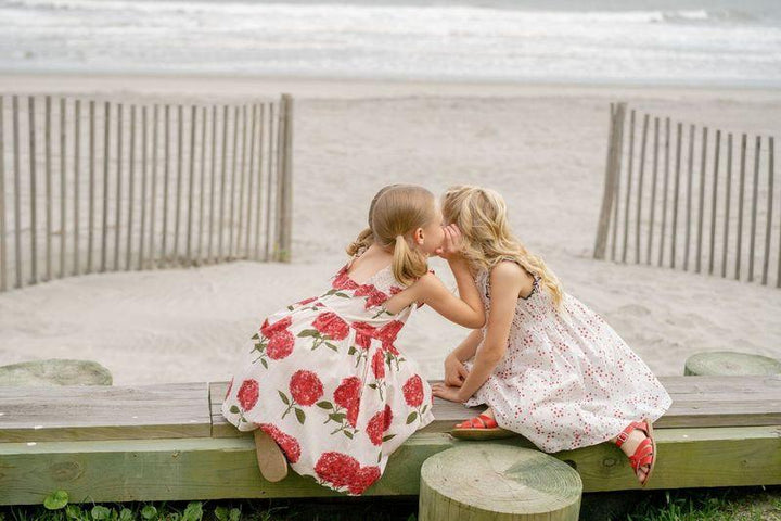 2 little girls whispering on the beach showing the pink hydrengea dress in natural light. 